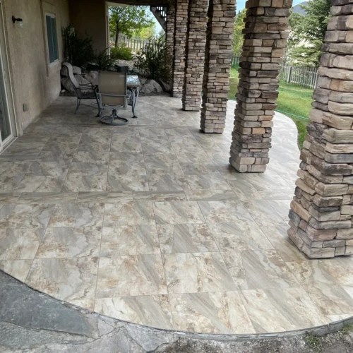 Covered outdoor patio in Peyton, CO, featuring large-format stone-look porcelain tiles and custom stacked stone pillar wraps by XCEL TILE.