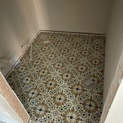Residential bathroom floor under construction featuring a complex, patterned cement-look tile held in place by red leveling clips in Parker, CO, by XCEL TILE.