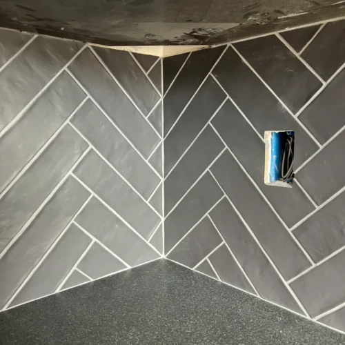 Close-up of a complex inside corner in Black Forest, CO, featuring dark grey ceramic tiles laid in a precise herringbone pattern by XCEL TILE.