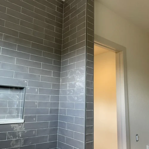 Close-up of a perfectly plumb outside corner on a shower wall, featuring glossy grey subway tile finished with a sleek metallic edge trim in Larkspur, CO, by XCEL TILE.