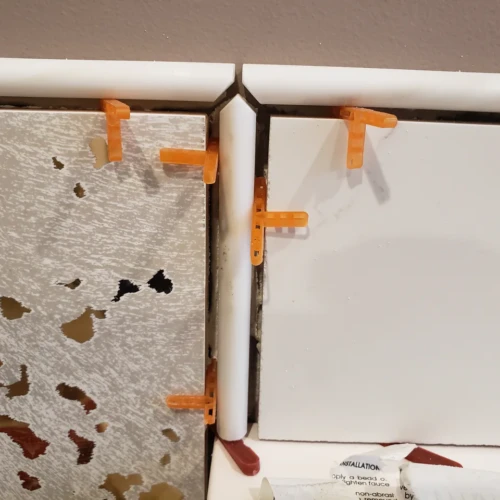 Close-up of a complex three-way tile corner in Parker, CO, being installed, featuring white tile, textured silver tile, and white bullnose trim pieces by XCEL TILE.