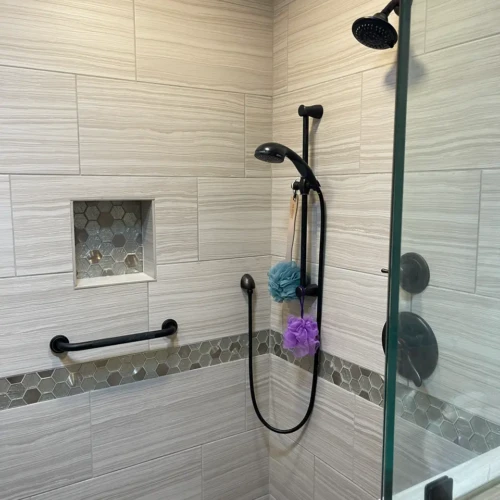Inside a custom glass shower enclosure in The Broadmoor, highlighting dual black shower fixtures, a recessed hexagon mosaic niche, and wood-look tile by XCEL TILE.