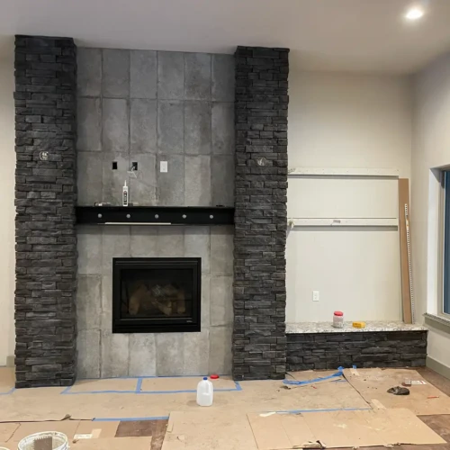 Large custom fireplace under construction in Larkspur, CO, featuring a smooth grey tile center flanked by two floor-to-ceiling columns of dark stacked stone by XCEL TILE.