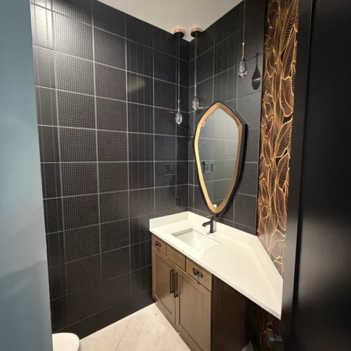 Modern powder room in Colorado Springs, CO, featuring a wall of textured matte black square tiles with subtle rivet detailing, a custom mirror, and dark vanity by XCEL TILE.