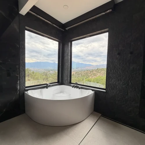Corner soaking tub in Colorado Springs, CO, surrounded by floor-to-ceiling textured dark slate-look porcelain accent walls framing large windows by XCEL TILE.