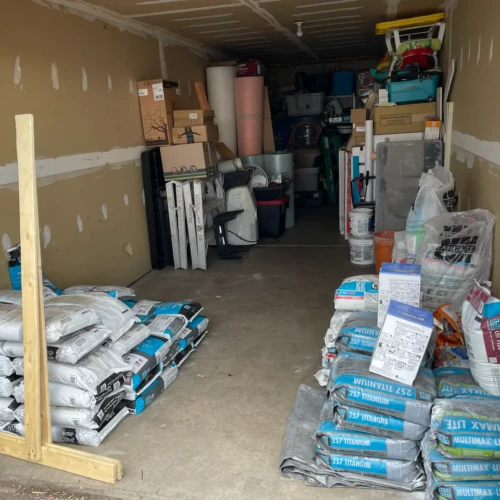 A well-organized storage space stocked with professional tile installation supplies, including stacks of Laticrete mortar bags, levels, and uncoupling membranes.