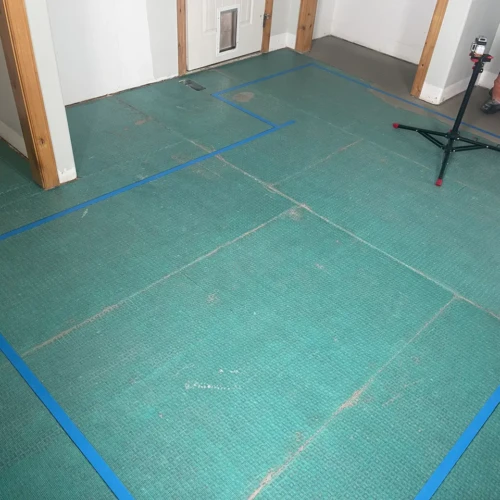 Subfloor preparation showcasing a green uncoupling membrane and blue layout tape for a custom floor tile installation in Colorado Springs, CO, by XCEL TILE.