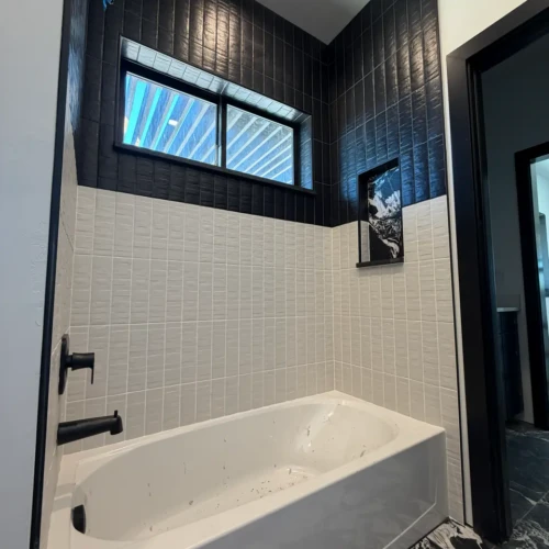 Modern bathtub surround in Colorado Springs, CO, featuring textured white vertical subway tiles on the lower half, bold black vertical subway tiles on top, and a custom recessed niche by XCEL TILE.