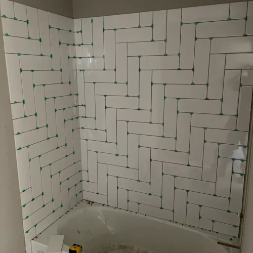 Bathtub surround under construction featuring white ceramic subway tiles laid in an inventive vertical herringbone pattern with green spacers in Colorado Springs, CO, by XCEL TILE.