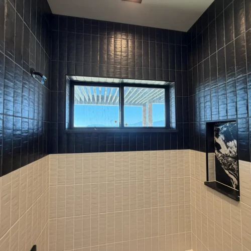 Custom bathtub surround in Colorado Springs, CO, highlighting black vertical subway tiles meticulously wrapped around an architectural window frame by XCEL TILE.