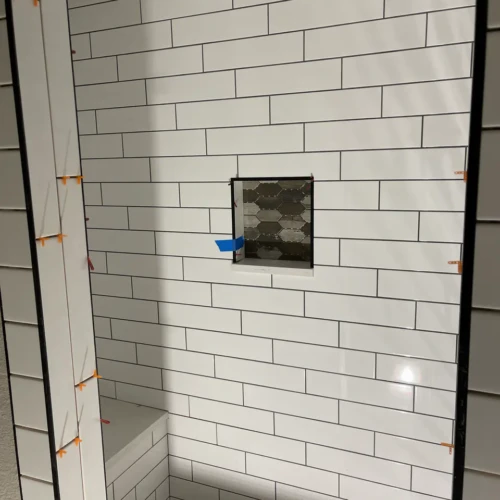 Shower wall under construction in Parker, CO, featuring white subway tile with dark contrasting grout and a recessed custom niche filled with dark hexagon mosaic tile by XCEL TILE.